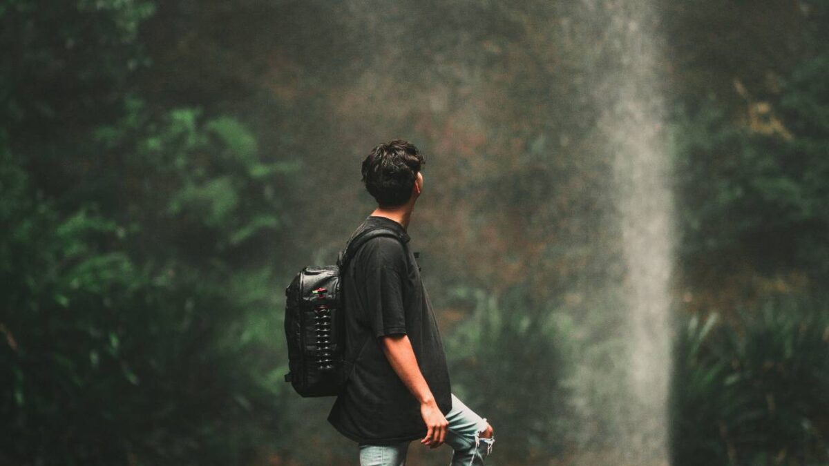 A digital nomad with a backpack looking at a waterfall