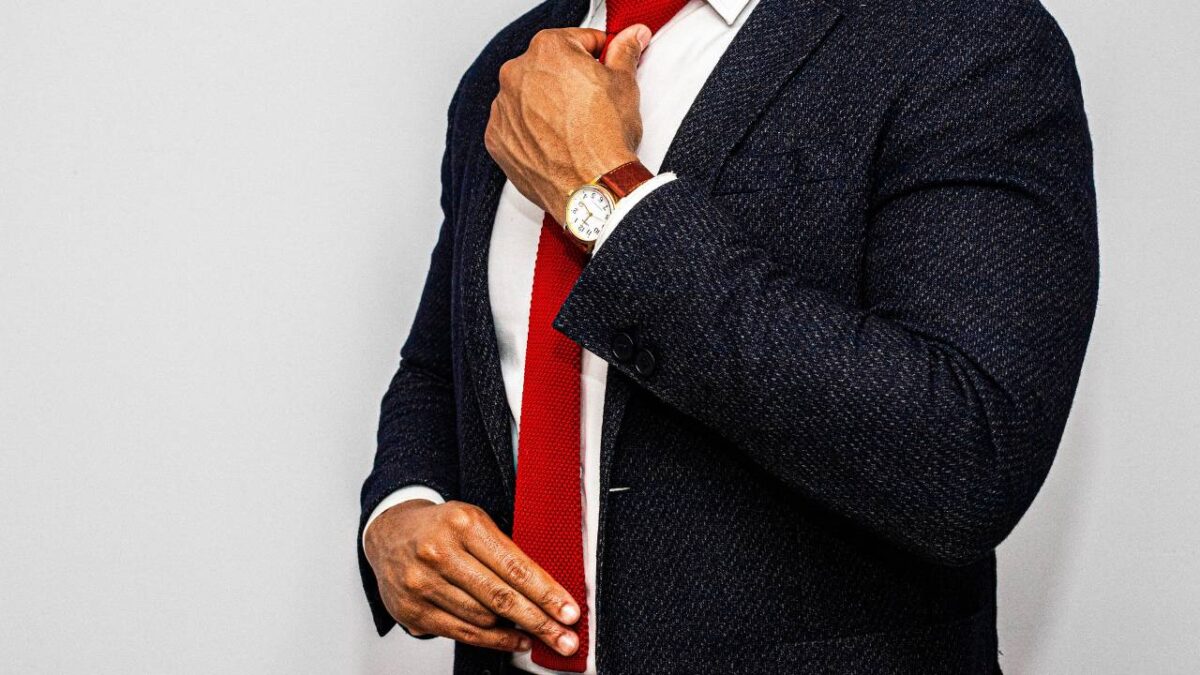 A man in a black suit adjusting his red tie