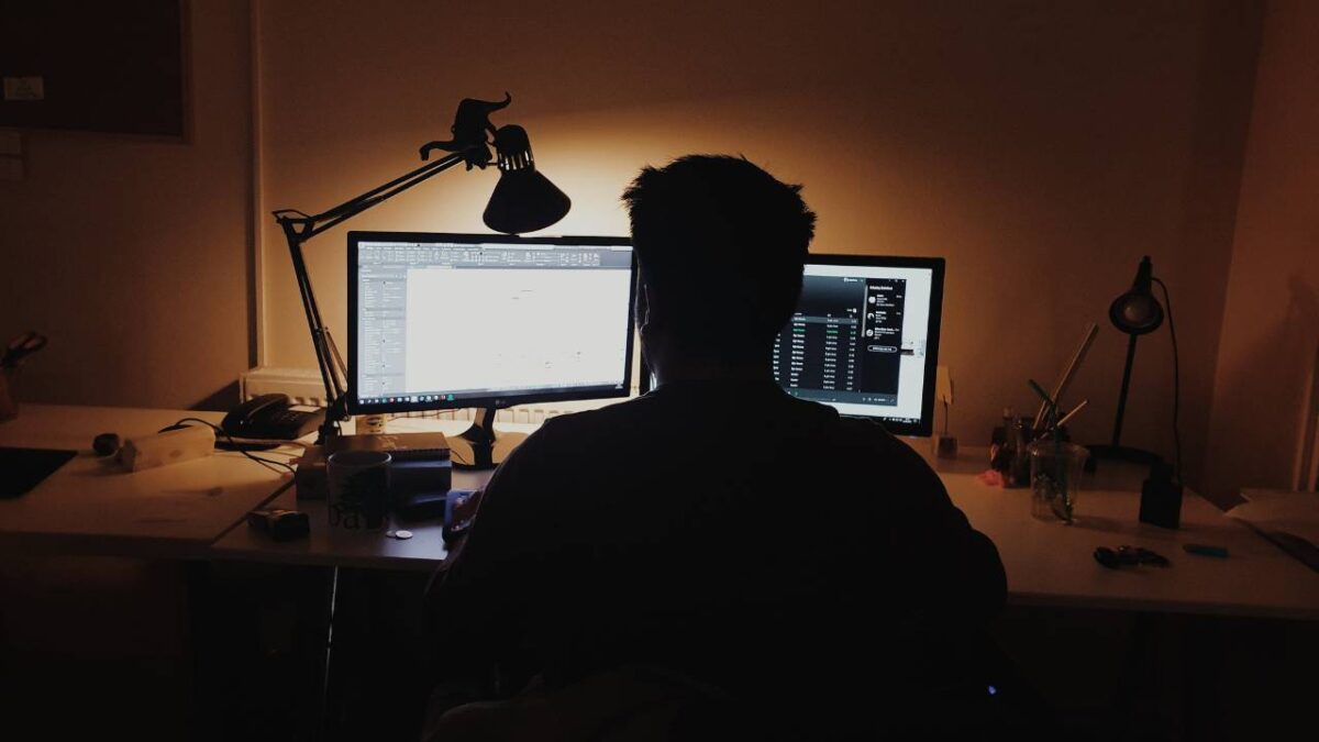 A man using a computer with two monitors in a dark room