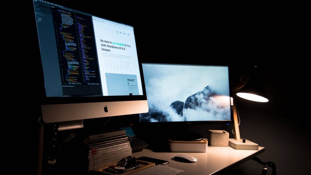 Two computer monitors on a table in the dark