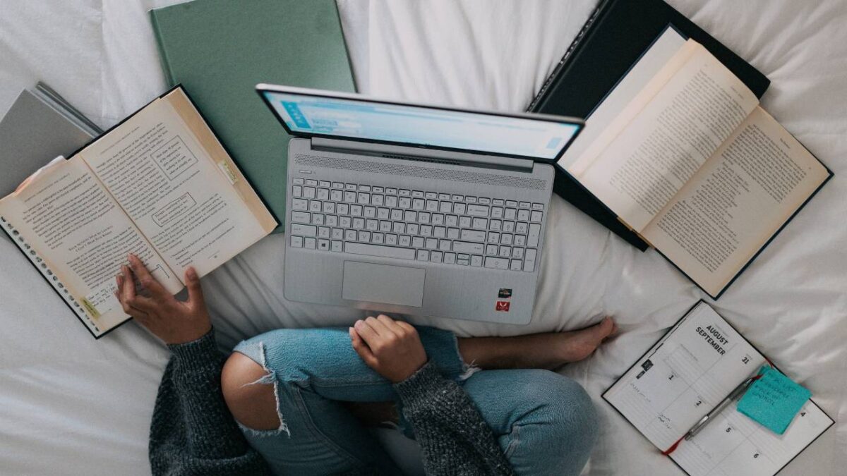 Woman conducting research on a bed with laptop and books