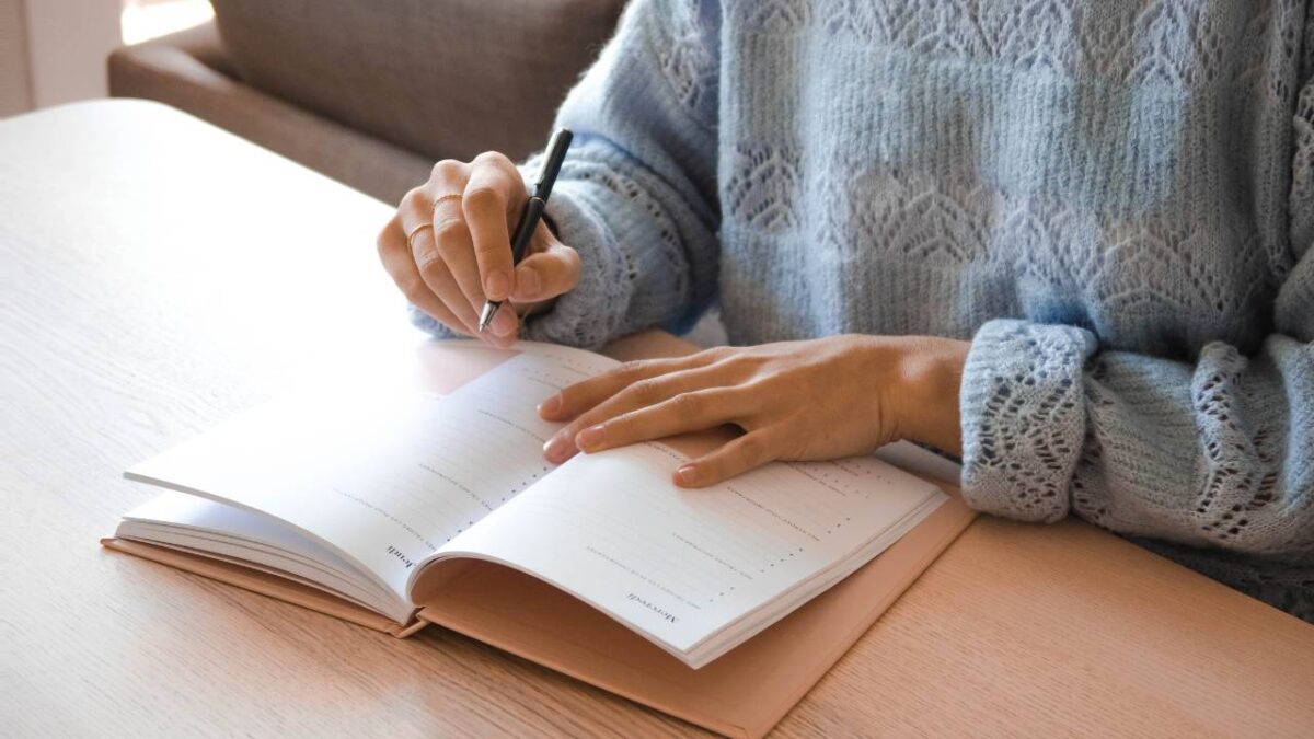 Woman in blue sweater writing in her notebook