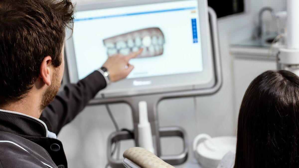 A dentist shows his patient a teeth model on a monitor