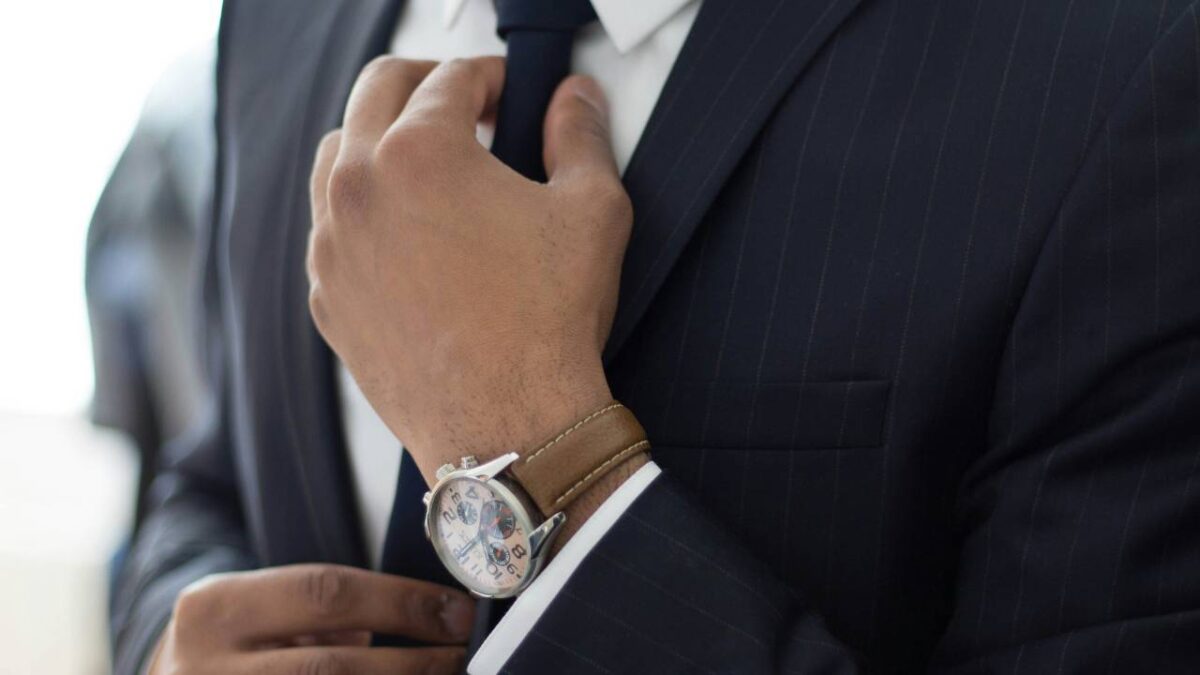 A closeup photo of a business person with a large watch typing up their tie