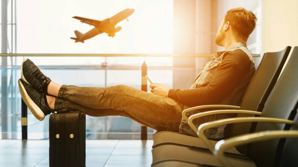 A man sitting in the airport looking at an airplane taking off
