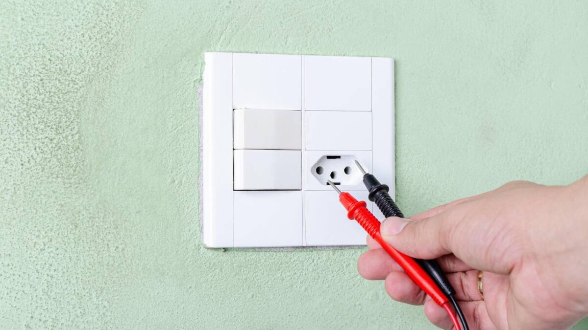 A photo of a man using test probes to check an electrical outlet
