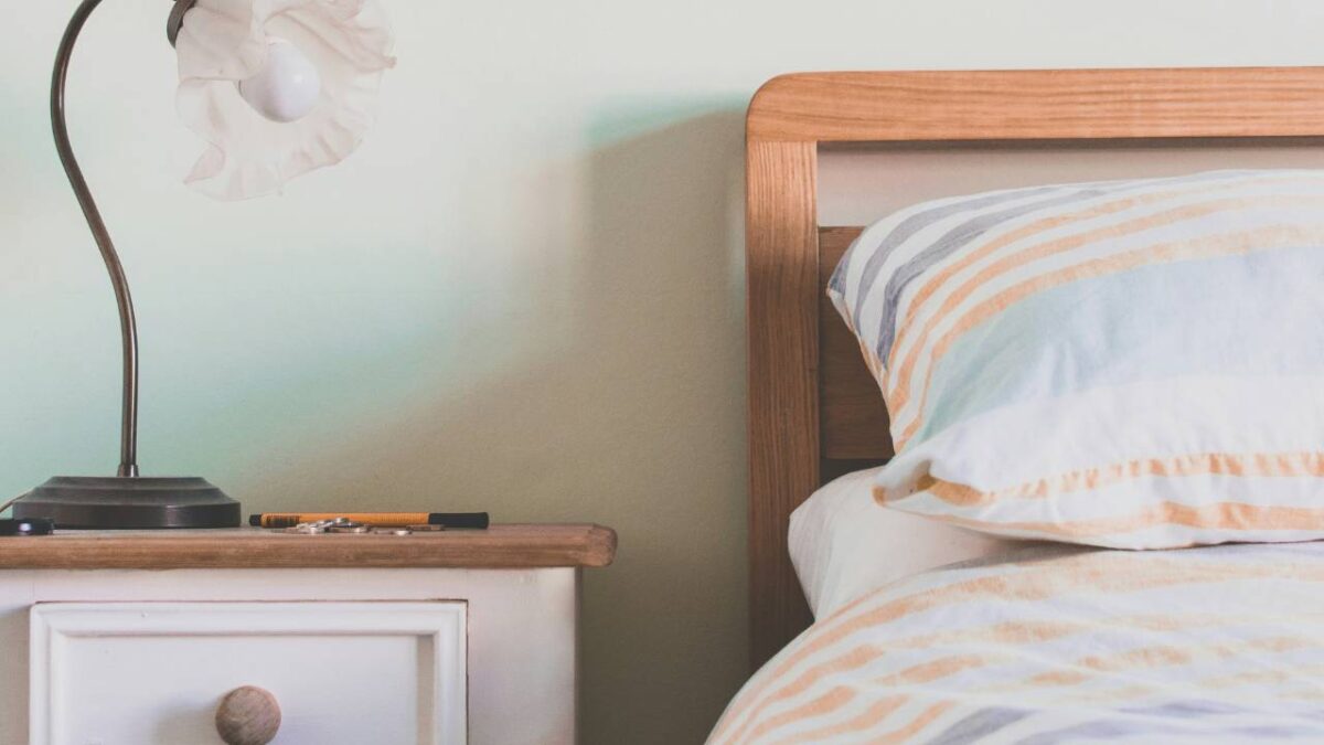 A photo of a nightstand with a lamp next to a comfortable bed